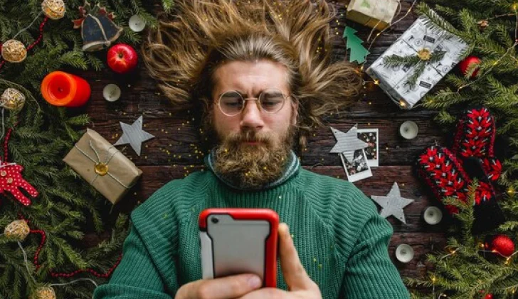 a guy checking his phone among Christmas gifts