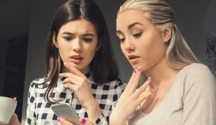 two girls checking phones looking surprised