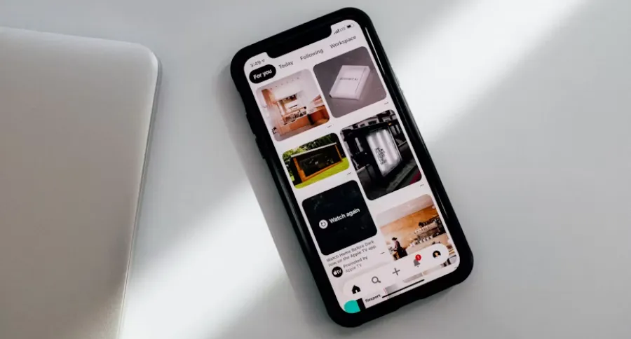 first page of pinterest on a mobile phone screen on a white table with a laptop beside it