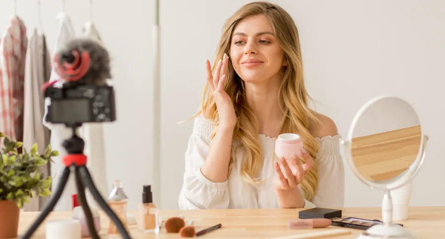a woman with long blond hair putting on face cream in front of a camera