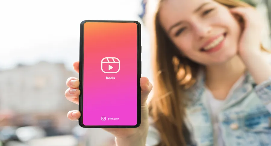 a woman showing her phone to the camera with the Instagram reels logo visible on it
