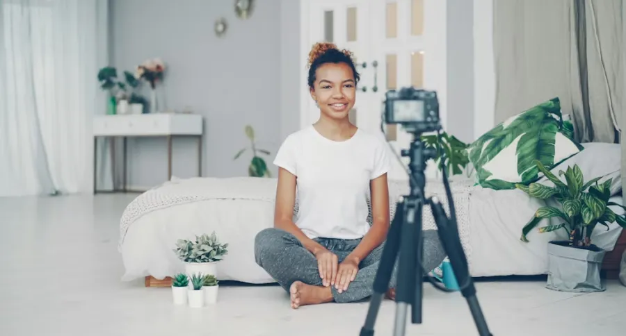 a woman filming in her bedroom while sitting on the floor with a camera on a tripod
