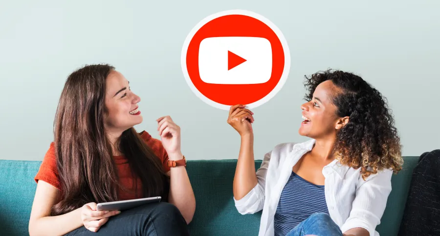 two women sitting on a couch talking about Youtube, one of them is holding a Youtube logo