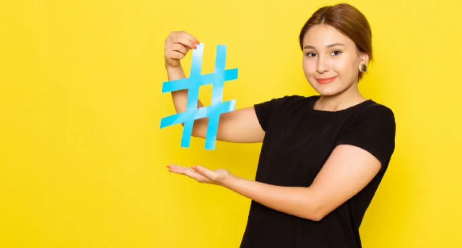 a woman in front of a yellow background holding a Hashtag symbol