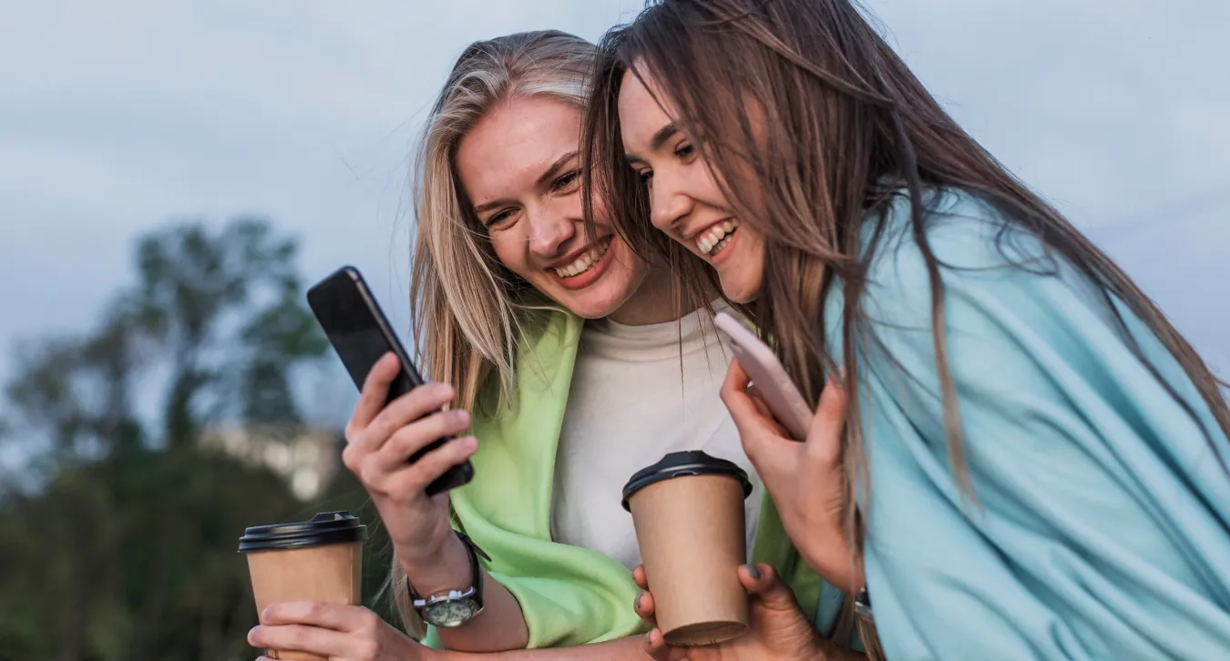 two women laughing at something while looking at their phone