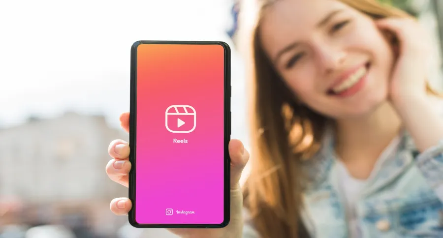 A woman showing Instagram Reel logo on a phone to the camera