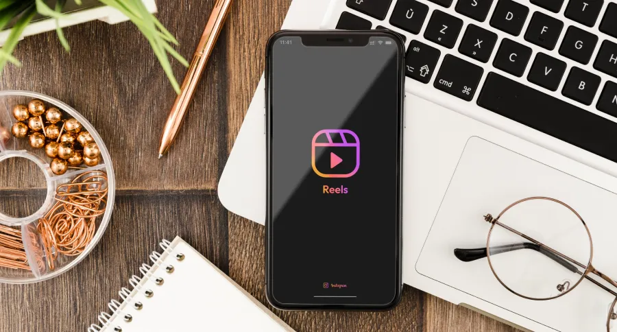 A woman on a laptop on a wooden desk showing Instagram Reel logo