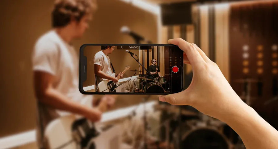 A hand holding a phone filming another person playing a guitar