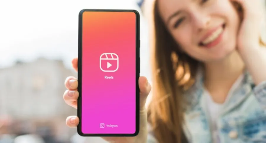 a woman holding a phone to the camera with the Instagram Reels logo showing on it